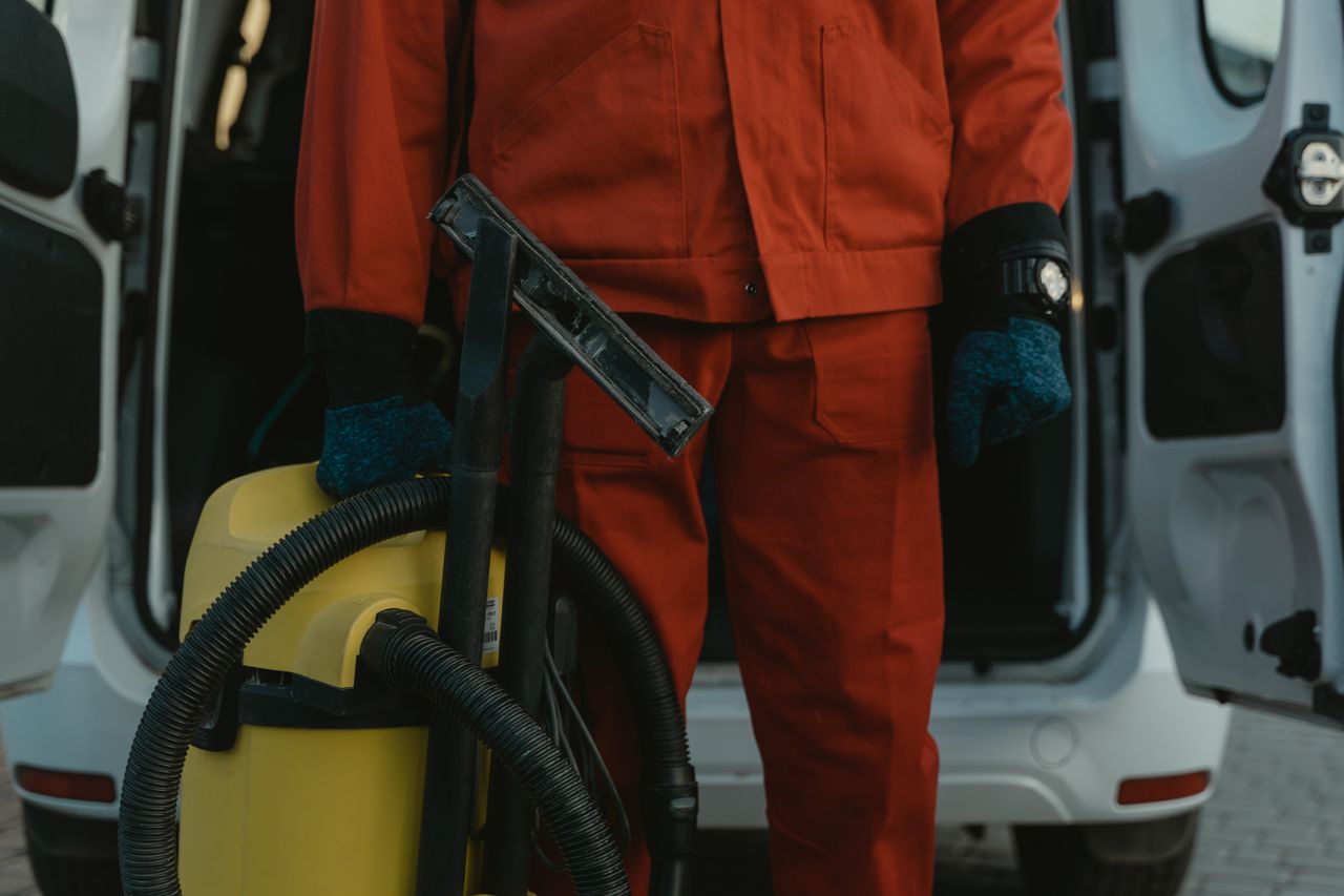 mobile-01 A professional cleaner in a red uniform holding a vacuum near a van, ready for service.